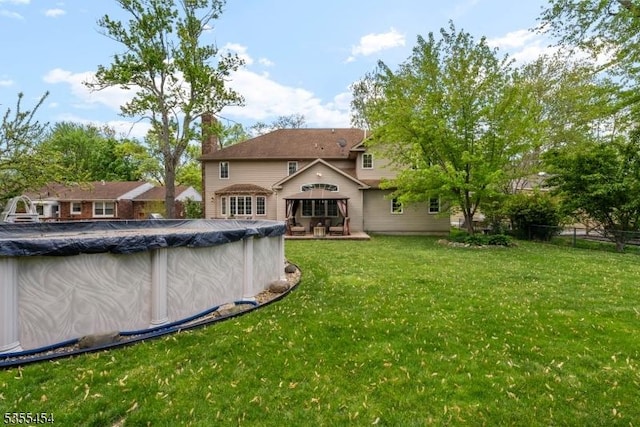 rear view of house with a chimney, fence, a yard, and a covered pool