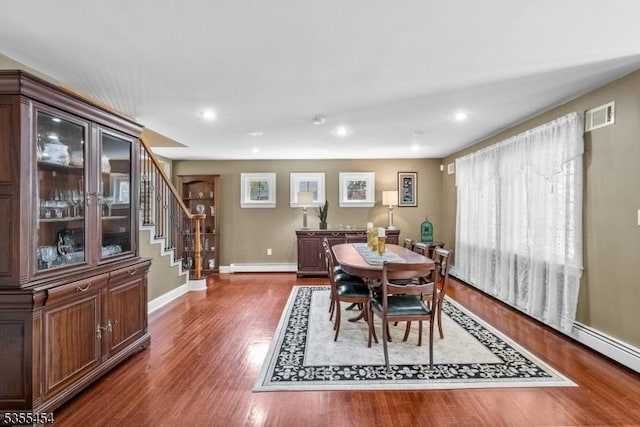 dining space with baseboards, wood finished floors, a baseboard radiator, visible vents, and stairway