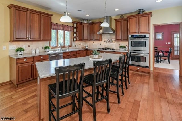 kitchen featuring a sink, open shelves, wall chimney exhaust hood, appliances with stainless steel finishes, and light wood-style floors