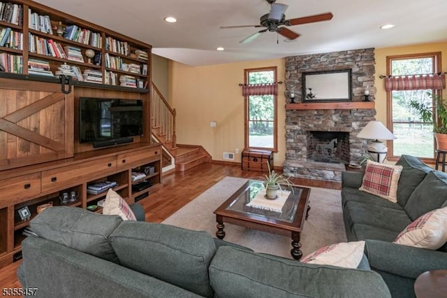 living area with wood finished floors, visible vents, a stone fireplace, ceiling fan, and stairs