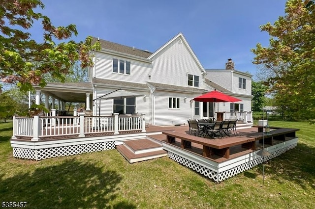 rear view of property with a yard, a chimney, a deck, and outdoor dining space