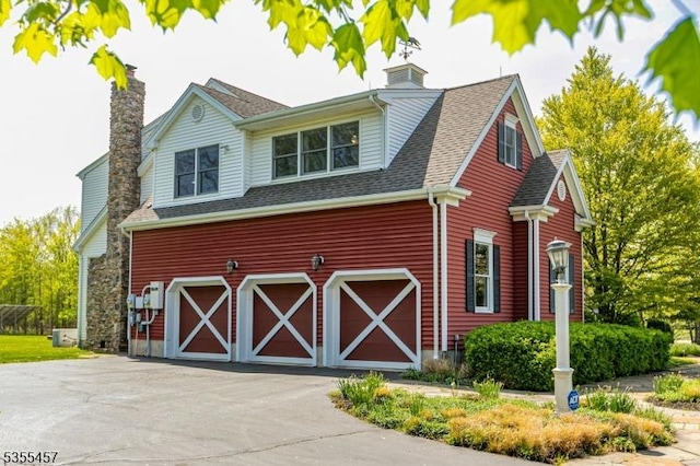 exterior space with an attached garage, a shingled roof, driveway, and a chimney