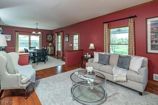 living area with an inviting chandelier, visible vents, wood finished floors, and crown molding