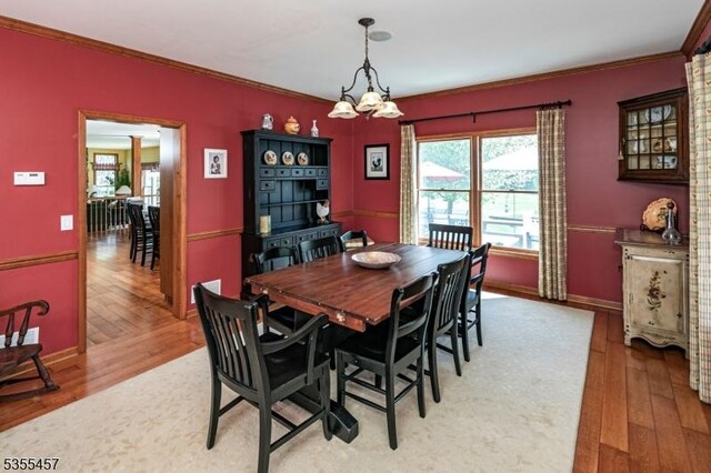 dining space with ornamental molding, a notable chandelier, light wood-style flooring, and baseboards