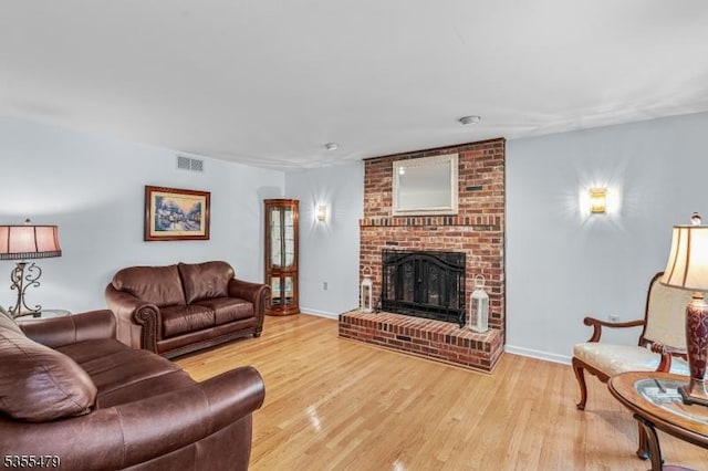 living area featuring light wood-type flooring, a brick fireplace, and baseboards