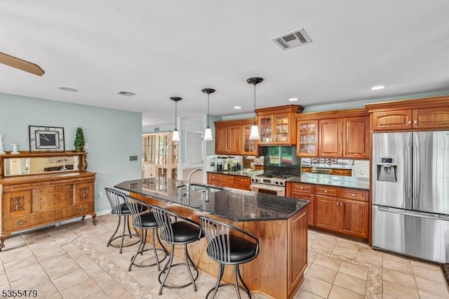 kitchen featuring appliances with stainless steel finishes, a sink, brown cabinetry, light tile patterned flooring, and a kitchen breakfast bar