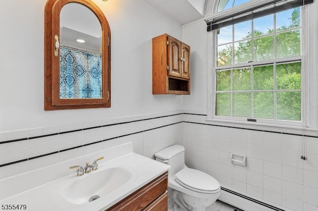 full bath with baseboard heating, tile walls, toilet, vanity, and a wainscoted wall