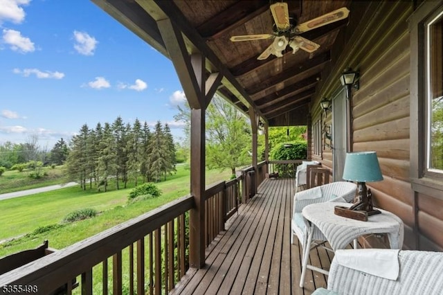 wooden deck featuring ceiling fan, a yard, and view of wooded area