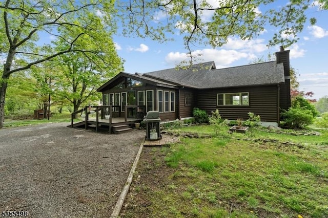 back of house featuring a wooden deck, a chimney, a sunroom, and roof with shingles