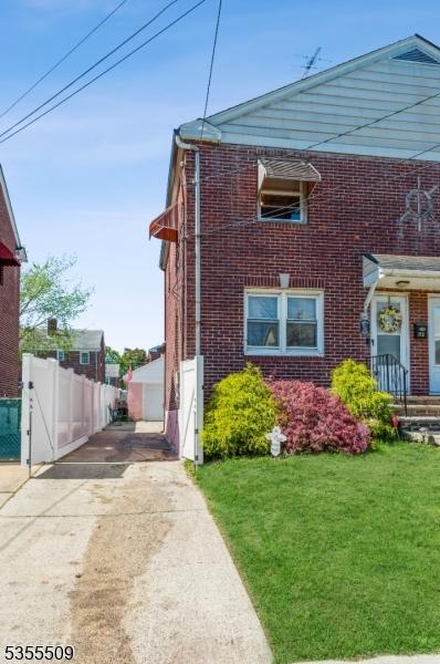 view of side of property featuring a lawn, fence, concrete driveway, and brick siding