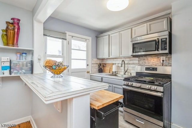 kitchen with gray cabinets, backsplash, a sink, baseboards, and stainless steel appliances