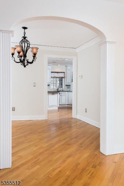 unfurnished dining area with arched walkways, a chandelier, light wood finished floors, and baseboards