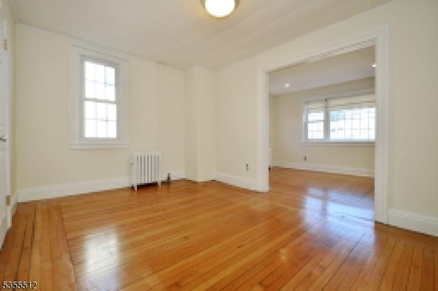 spare room with radiator heating unit, plenty of natural light, light wood-style floors, and baseboards