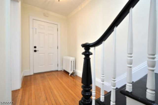 foyer entrance featuring radiator heating unit, ornamental molding, and light wood-style floors