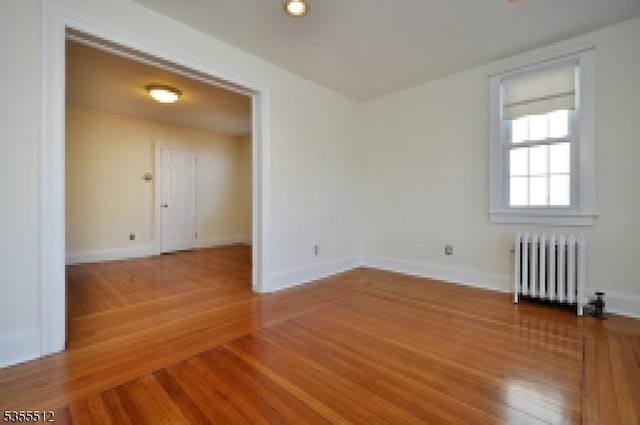 empty room featuring radiator, wood finished floors, and baseboards