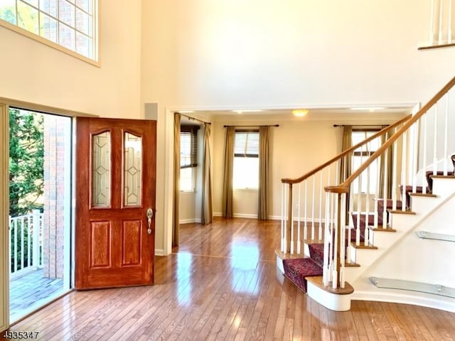 entryway featuring a towering ceiling, stairs, hardwood / wood-style flooring, and baseboards