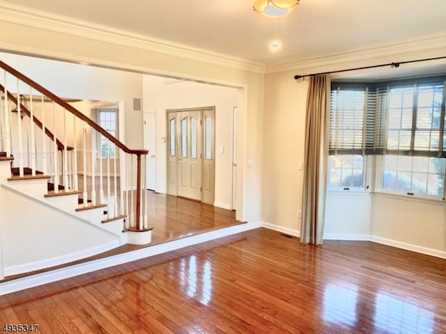 empty room featuring crown molding, wood finished floors, baseboards, and stairway
