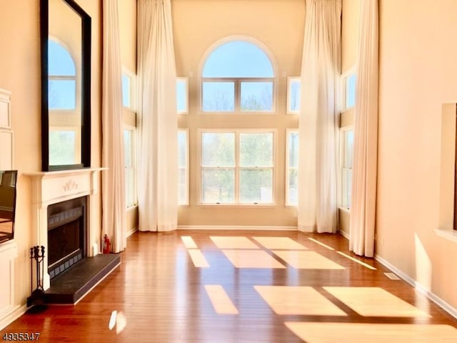 unfurnished living room featuring wood finished floors, a high ceiling, a fireplace with raised hearth, and baseboards