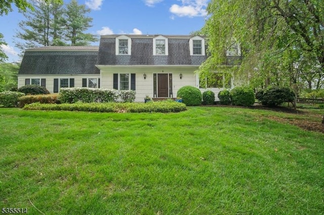 colonial inspired home with mansard roof, a shingled roof, and a front yard