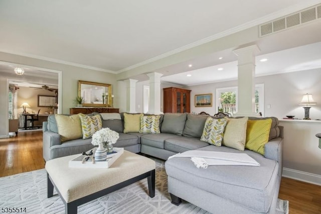 living room with decorative columns, wood finished floors, ornamental molding, baseboards, and recessed lighting