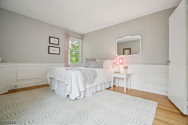 bedroom featuring light wood-style floors, wainscoting, and a decorative wall