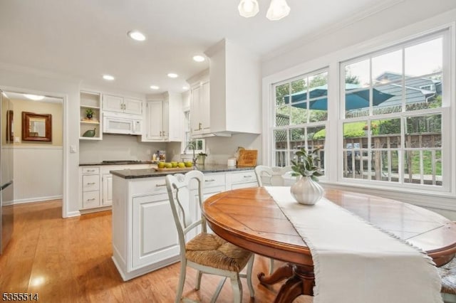 kitchen with white microwave, crown molding, white cabinetry, dark countertops, and light wood-style flooring