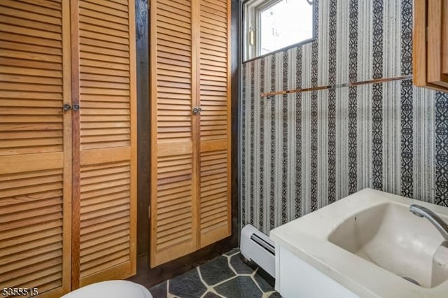 bathroom with baseboard heating, a sink, a closet, toilet, and wallpapered walls