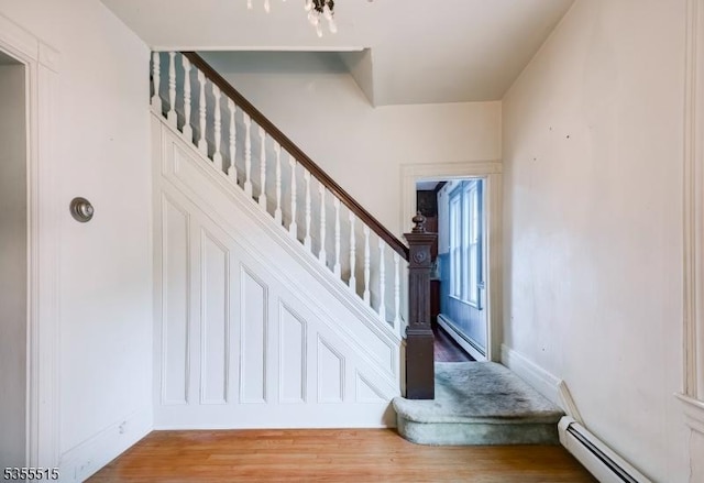 stairway featuring wood finished floors, baseboards, a baseboard heating unit, and baseboard heating