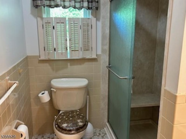bathroom featuring tile walls, a shower stall, toilet, and wainscoting