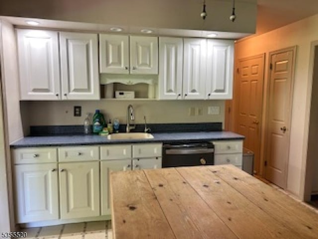 kitchen featuring a sink, dishwashing machine, white cabinets, and dark countertops