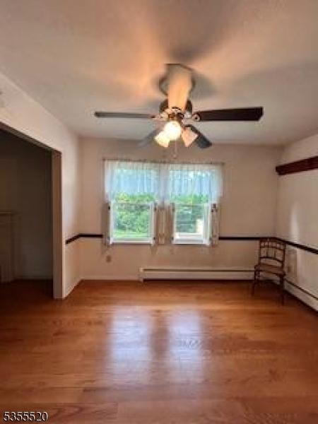 unfurnished bedroom with a baseboard heating unit, wood finished floors, baseboards, and a ceiling fan