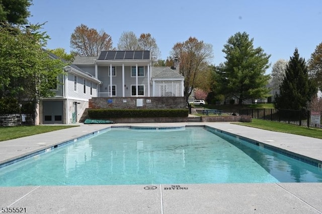 back of property with roof mounted solar panels, stairs, a chimney, and fence