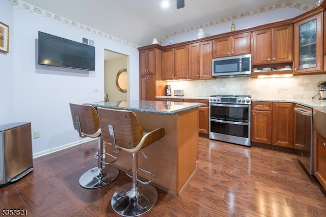 kitchen with stainless steel appliances, dark wood-style floors, brown cabinetry, lofted ceiling, and a kitchen breakfast bar