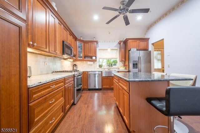 kitchen featuring appliances with stainless steel finishes, a breakfast bar, dark wood-style floors, decorative backsplash, and brown cabinets