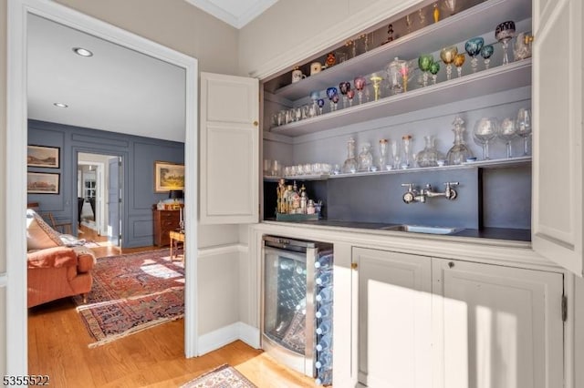 bar featuring ornamental molding, a sink, beverage cooler, light wood-type flooring, and a dry bar