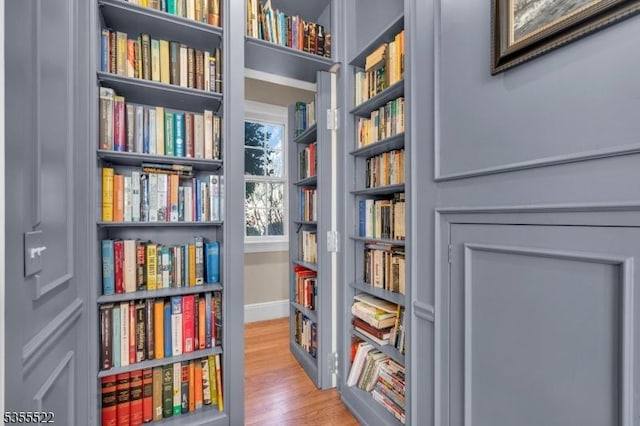 living area with baseboards, bookshelves, and wood finished floors