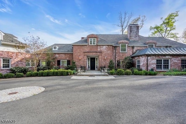 view of front of property featuring brick siding, a chimney, and a standing seam roof