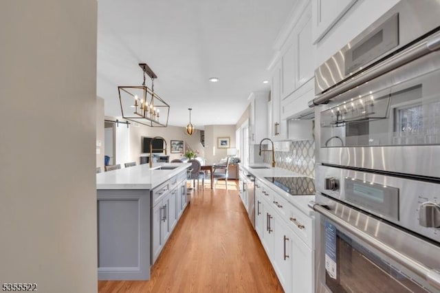 kitchen with white cabinets, stainless steel double oven, light wood finished floors, and black electric stovetop