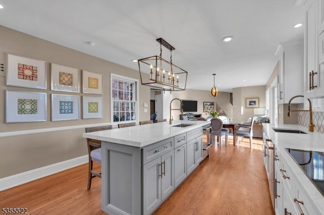 kitchen with a sink, gray cabinets, a center island with sink, and light wood-type flooring