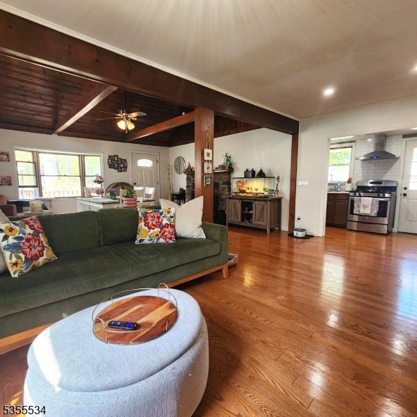 living area featuring a ceiling fan, wood finished floors, and beamed ceiling