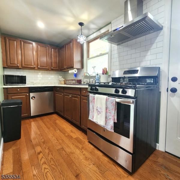 kitchen with wall chimney range hood, appliances with stainless steel finishes, light wood-style flooring, and a sink