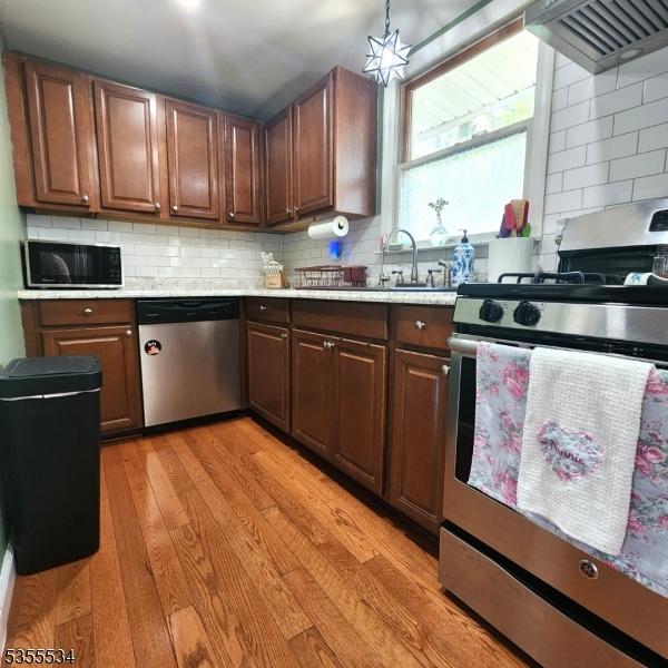 kitchen featuring backsplash, appliances with stainless steel finishes, light wood-type flooring, light countertops, and custom range hood