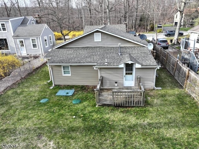 rear view of house featuring a yard, fence, and a shingled roof