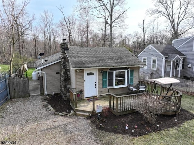 view of front of property with fence, roof with shingles, a chimney, and a deck