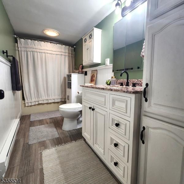 bathroom featuring toilet, wood finished floors, vanity, baseboard heating, and shower / tub combo