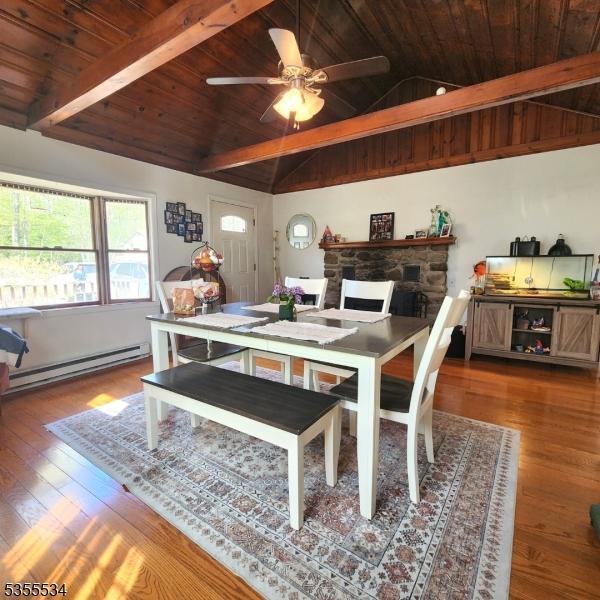 dining area with wood finished floors, a stone fireplace, baseboard heating, vaulted ceiling with beams, and wood ceiling