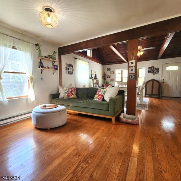 living room with wood-type flooring, a baseboard radiator, lofted ceiling with beams, and a wealth of natural light