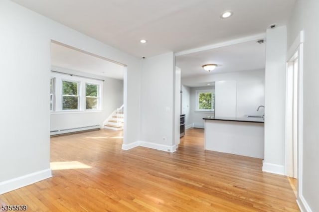 unfurnished living room featuring baseboard heating, light wood-type flooring, stairs, recessed lighting, and baseboards