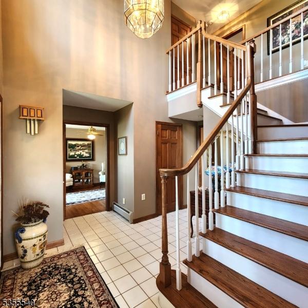 202 Fredon Springdale Rd, Fredon Twp, NJ 07860 - stairway with a notable chandelier, a baseboard radiator, baseboards, tile patterned floors, and a high ceiling