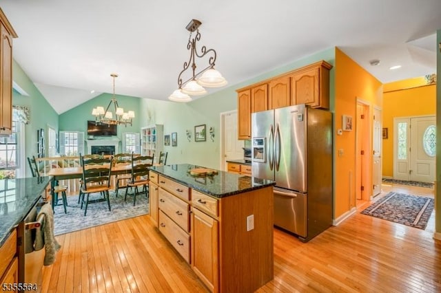 kitchen featuring stainless steel refrigerator with ice dispenser, light wood-type flooring, dark stone counters, a center island, and pendant lighting